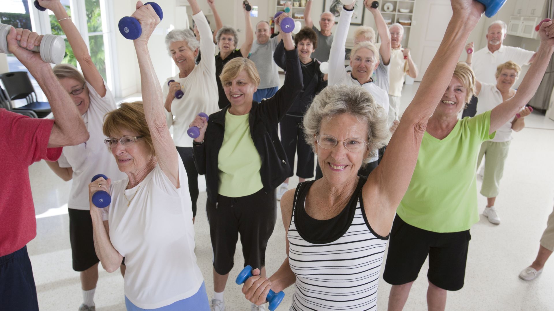 Grupa starszych osób wykonuje ćwiczenia dla seniorów na siłowni.