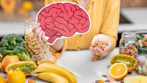 Dieta dla mózgu - kobieta z rysunkiem mózgu w dłoni jest otoczona pokarmami dobrymi dla jego funkcjonowania.