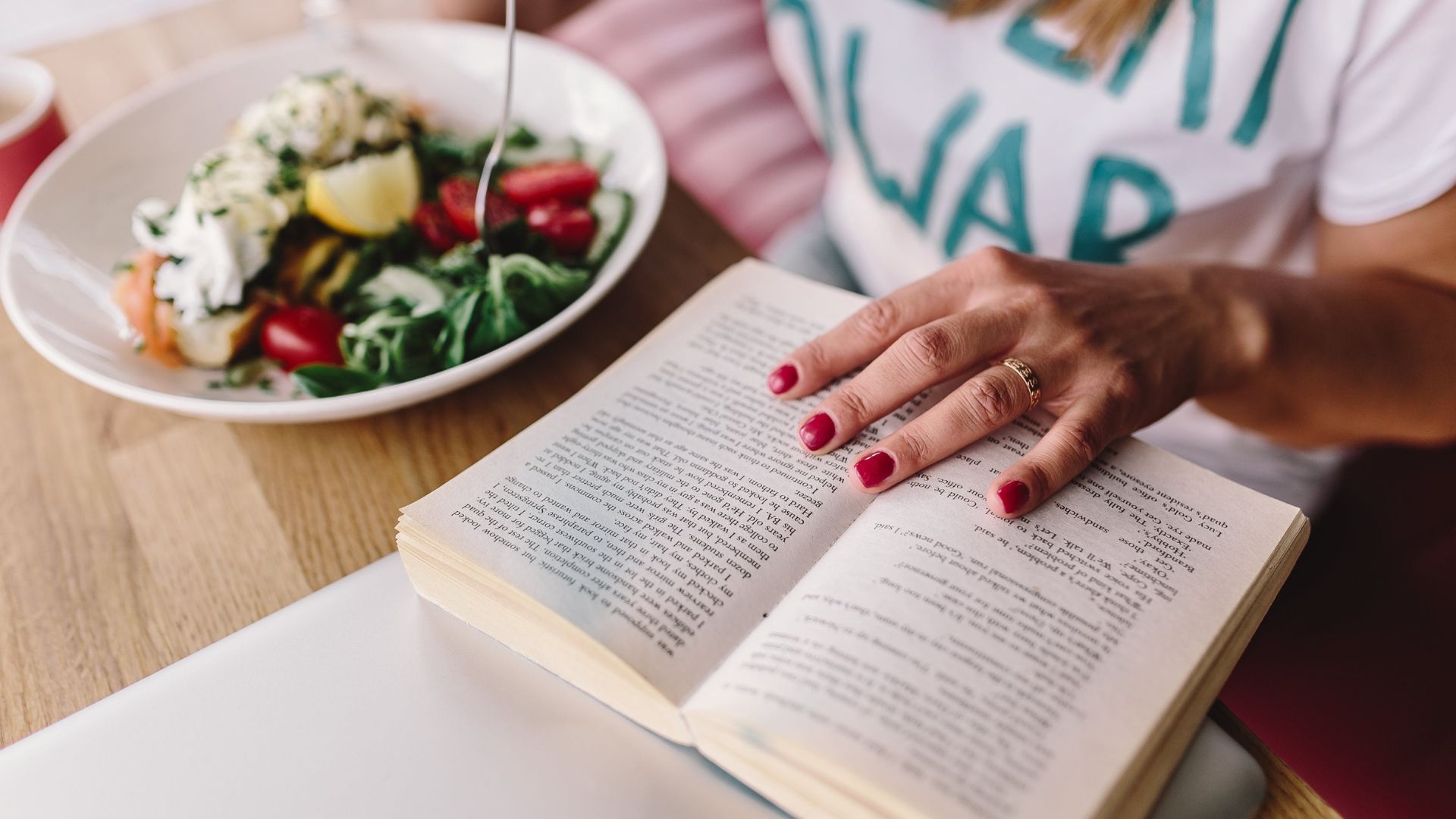 Kobieta czyta książki o zdrowym odżywianiu przy obiedzie.