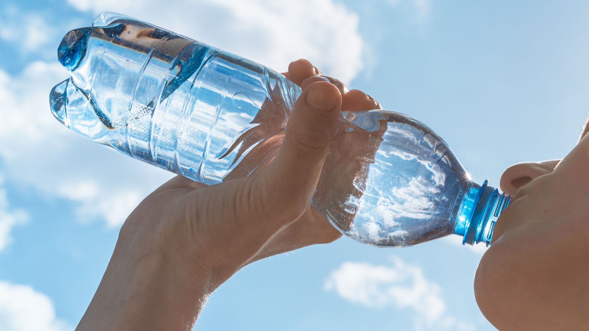 Picie wody przedstawione w koncepcji kobiety, która bierze łyk wody z plastikowej butelki na tle nieba.