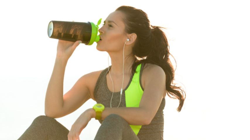 Aktywność fizyczna a depresja – jak są powiązane? Na zdjęciu młoda kobieta poje wodę w przerwie podczas biegania.