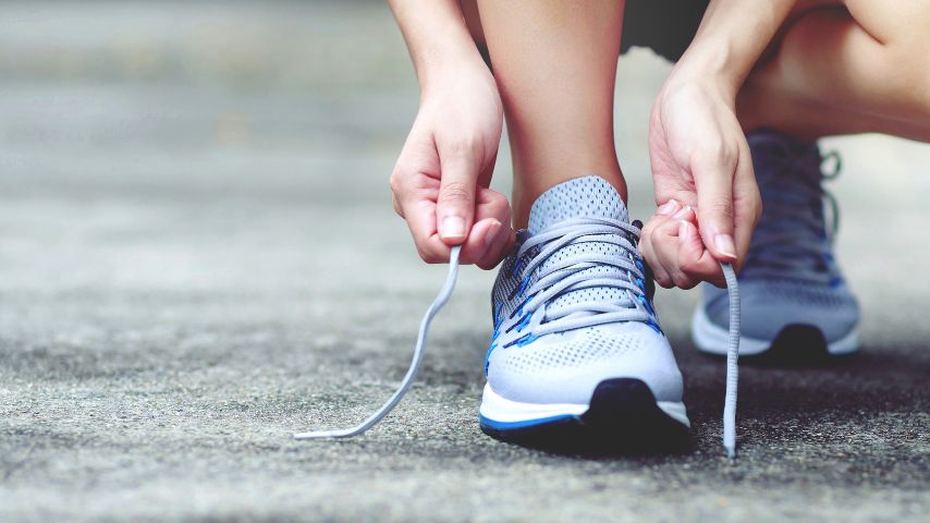 Biegacz zawiązuje sznurowadła w swoich butach do biegania, aby zadbać o zdrowie stóp.