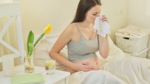 Kobieta, która cierpi na przeziębienie w ciąży, leży w łóżku.